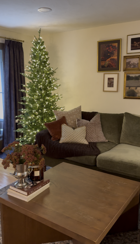 7.5 ft slim Grand Duchess twinkling Christmas tree with warm white LED lights styled in a cozy living room corner with green sectional and gallery wall art.
