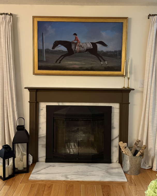 Samsung Frame TV displaying vintage equestrian horse art in a gold Deco Frame, styled above a brown fireplace mantel with marble surround and lantern decor.