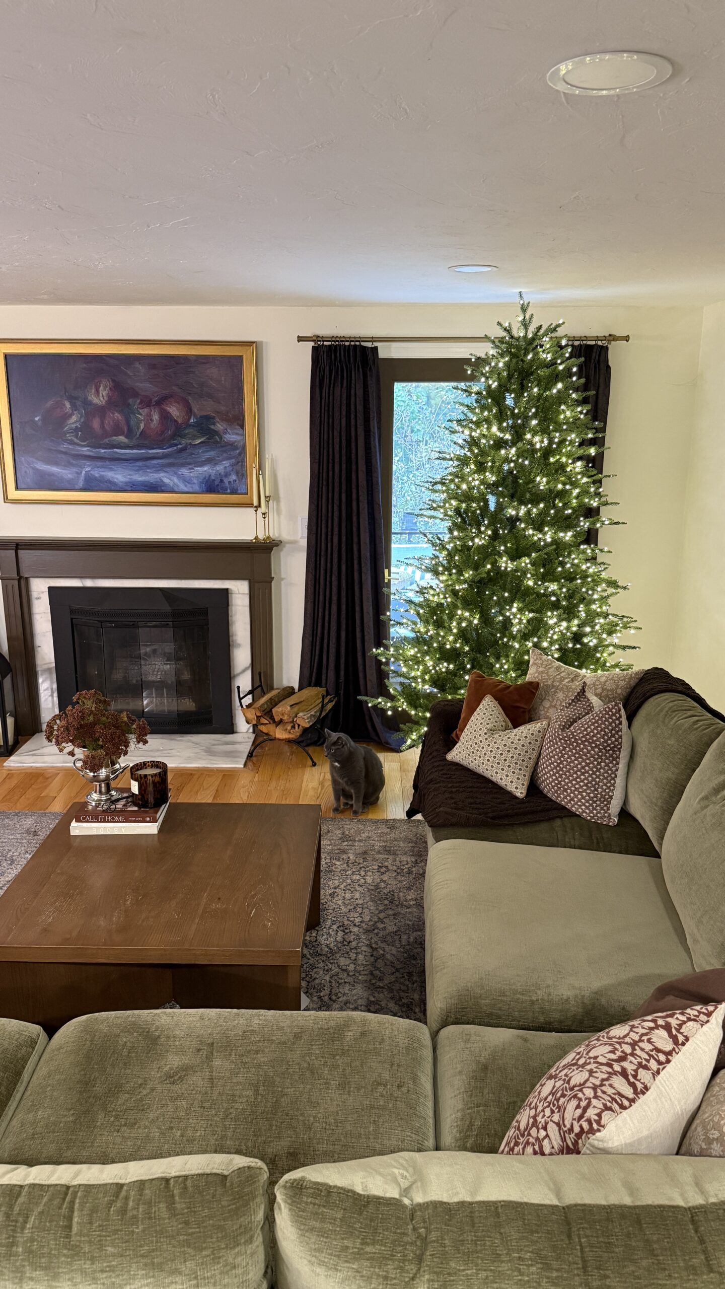 7.5 ft regular width Grand Duchess twinkling Christmas tree with warm white LED lights in a cozy living room with fireplace and green sectional sofa.