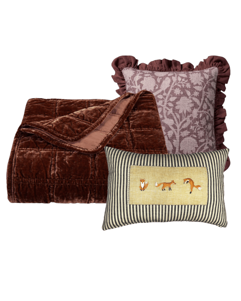A cozy fall throw combination featuring a rich brown velvet blanket, mauve floral pillow with ruffled edges, and a striped pillow embroidered with foxes — perfect for creating a whimsical, warm, woodland-inspired home.