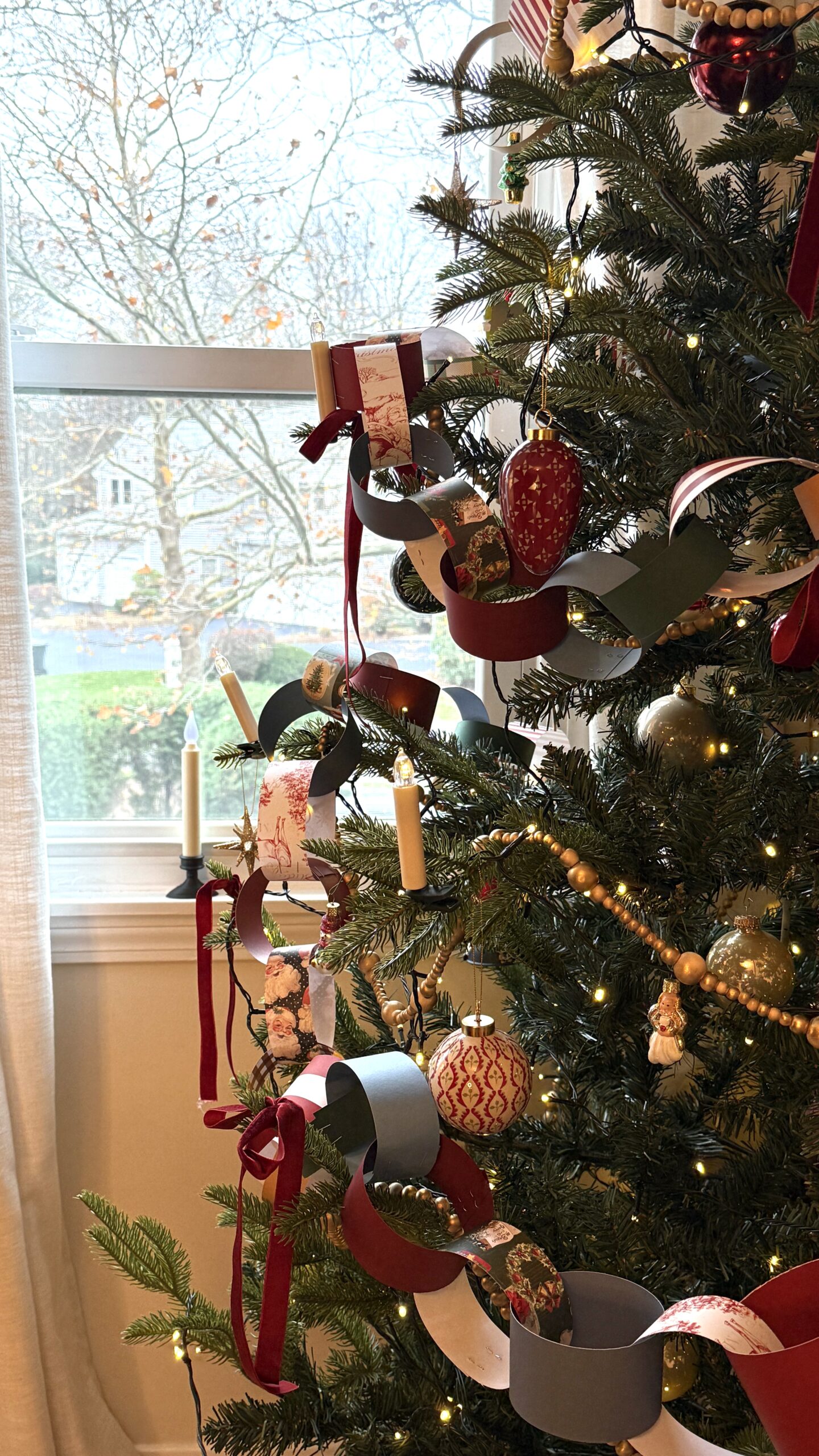 Nostalgic Christmas tree with handmade paper chain garland, red and gold ornaments, bead garland, and candle lights creating a whimsical and cozy holiday look.