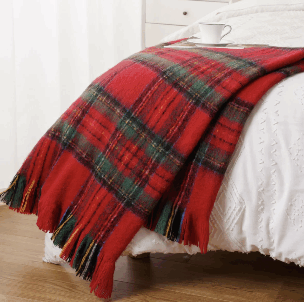 Soft red tartan plaid throw blanket draped on a bed, adding nostalgic Christmas warmth and classic cozy texture.