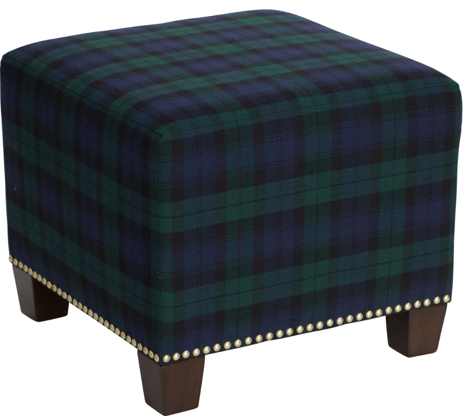 Small upholstered ottoman in dark green tartan plaid, used as an accent seat to add traditional pattern and cozy character to a living room."