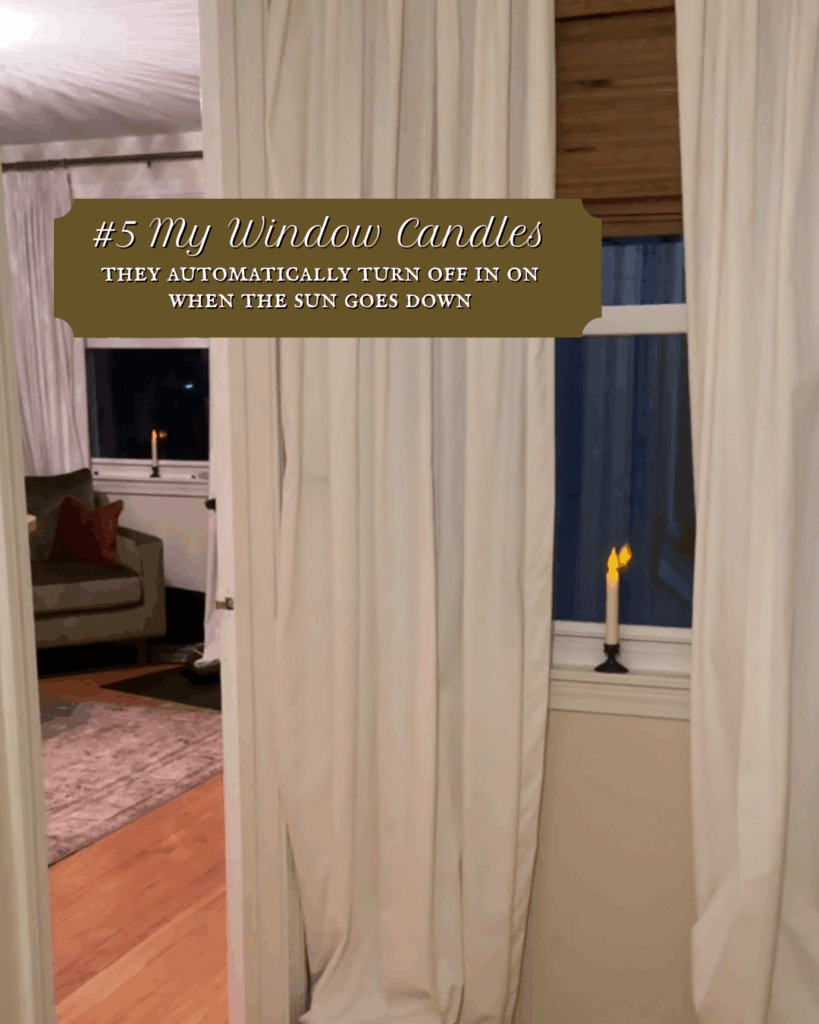 Battery-operated window candle glowing at dusk behind sheer white curtains in a cozy living room.