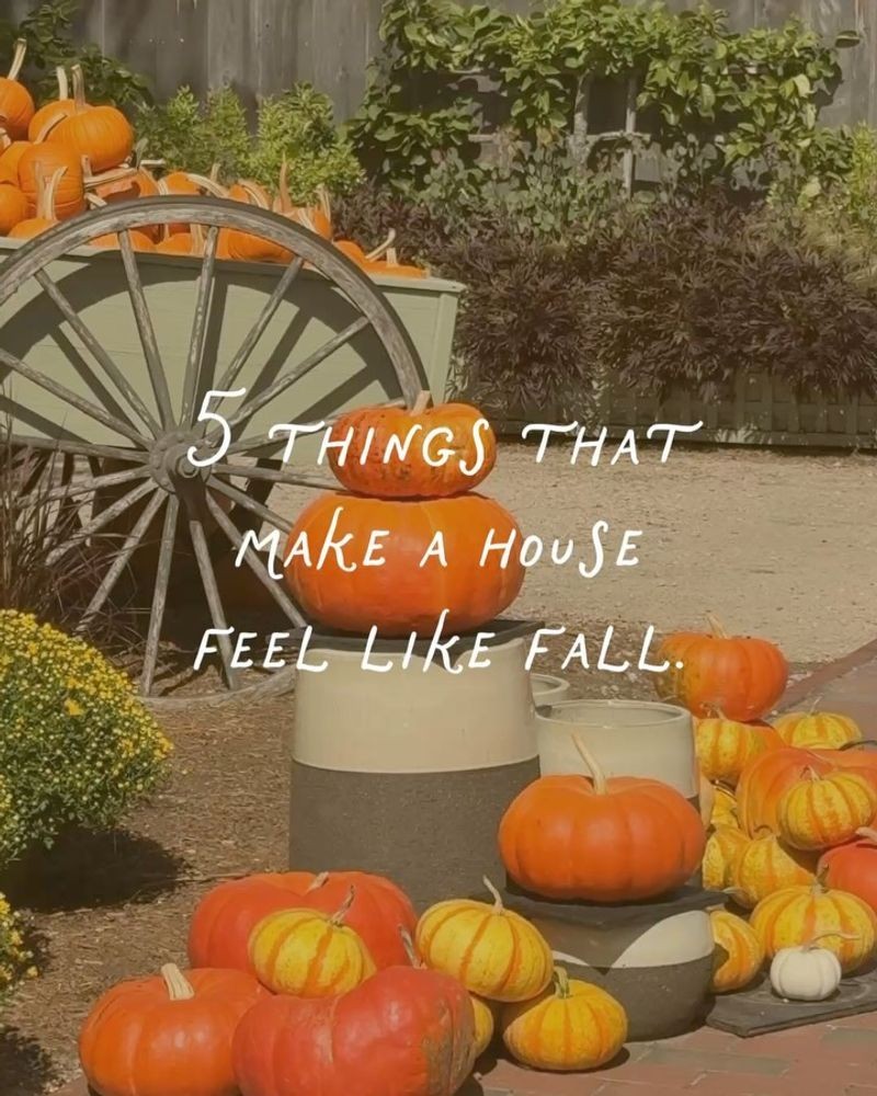 Pumpkins stacked by a wagon wheel on a New England farm with the words 5 things that make a house feel like fall