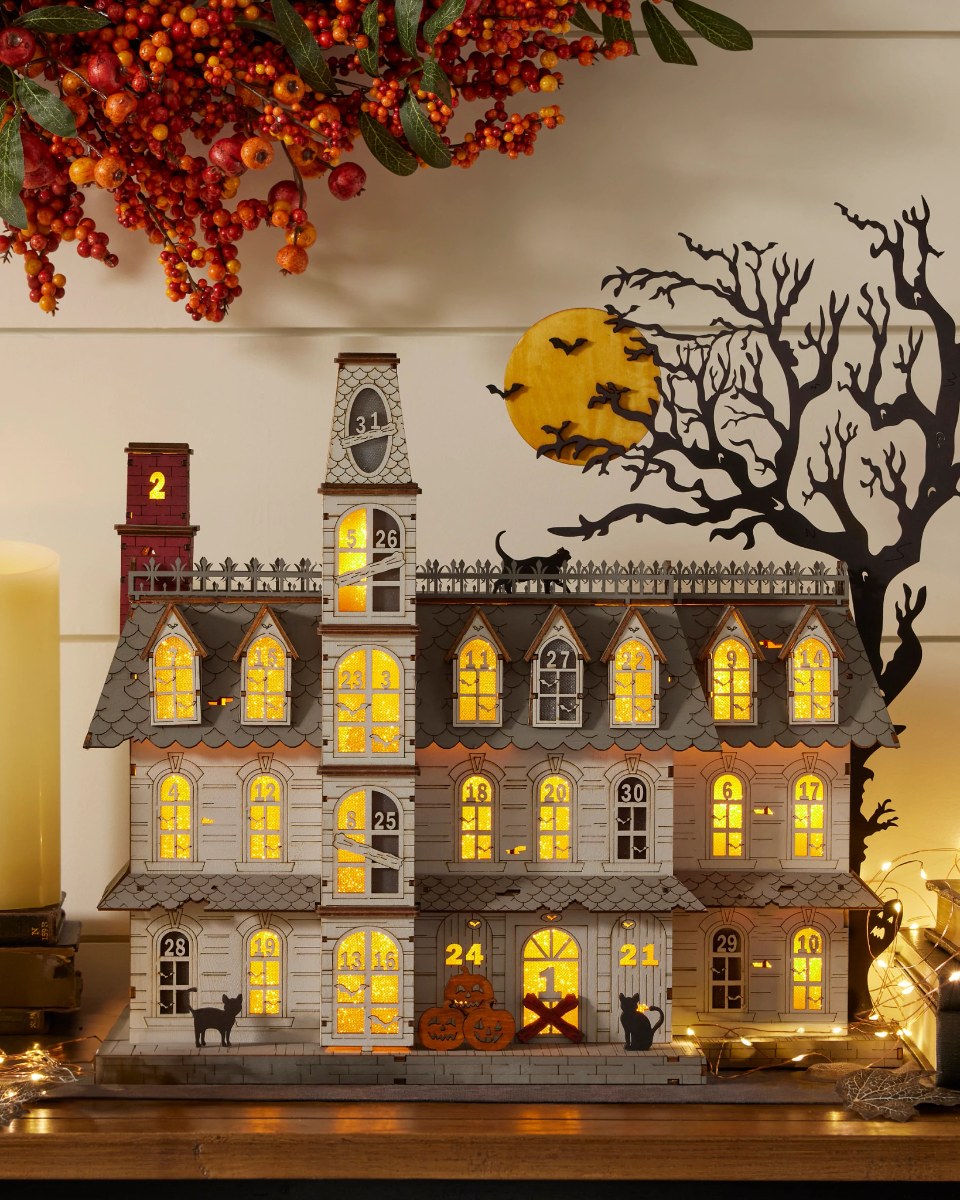 Lit wooden Halloween countdown calendar Spooky Manor glowing on a mantel